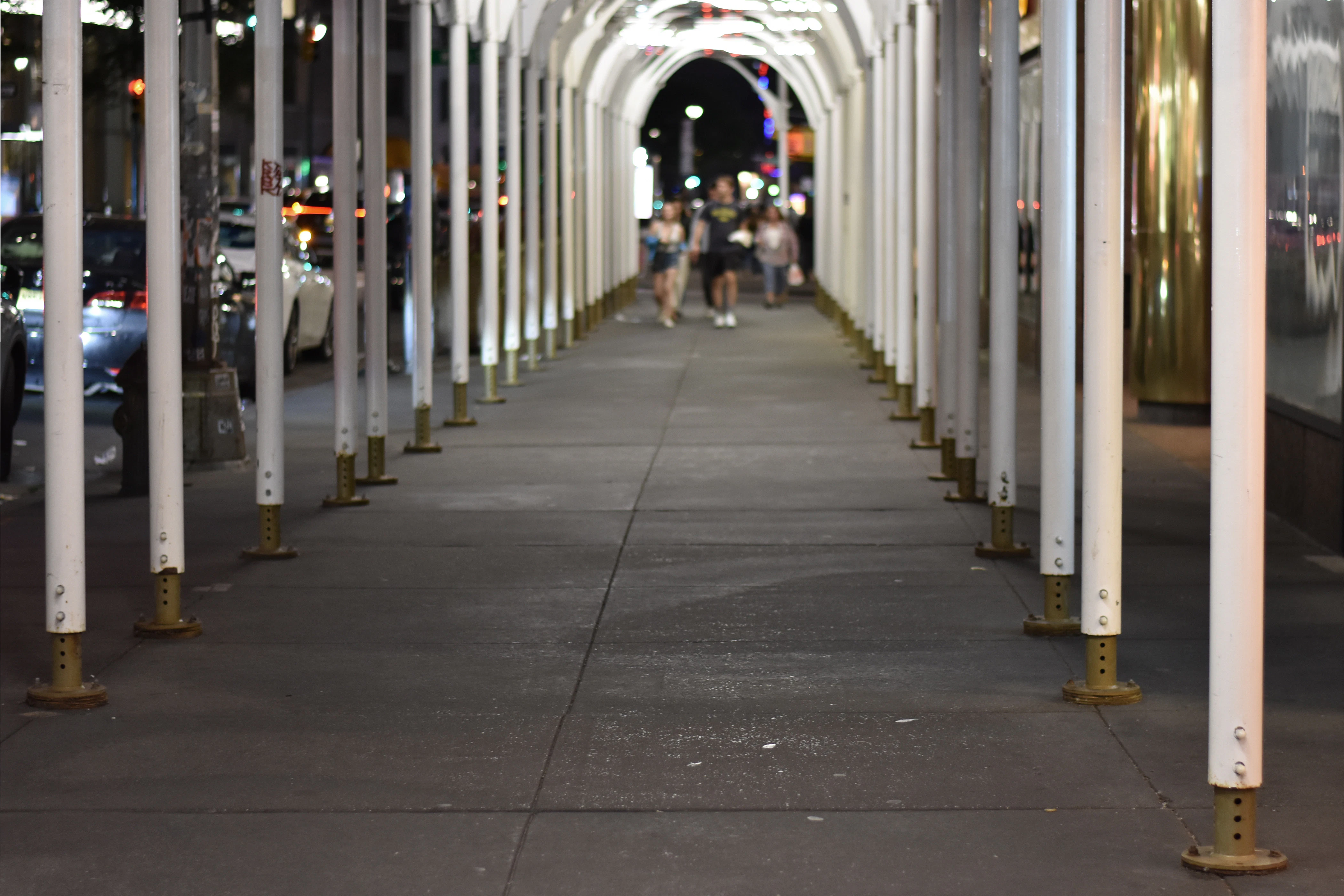Pedestrians walk through a temporary NYC sidewalk shed at sunset, illustrating updated compliance with Local Law 48 and Local Law 51 of 2025 on safety and visibility.