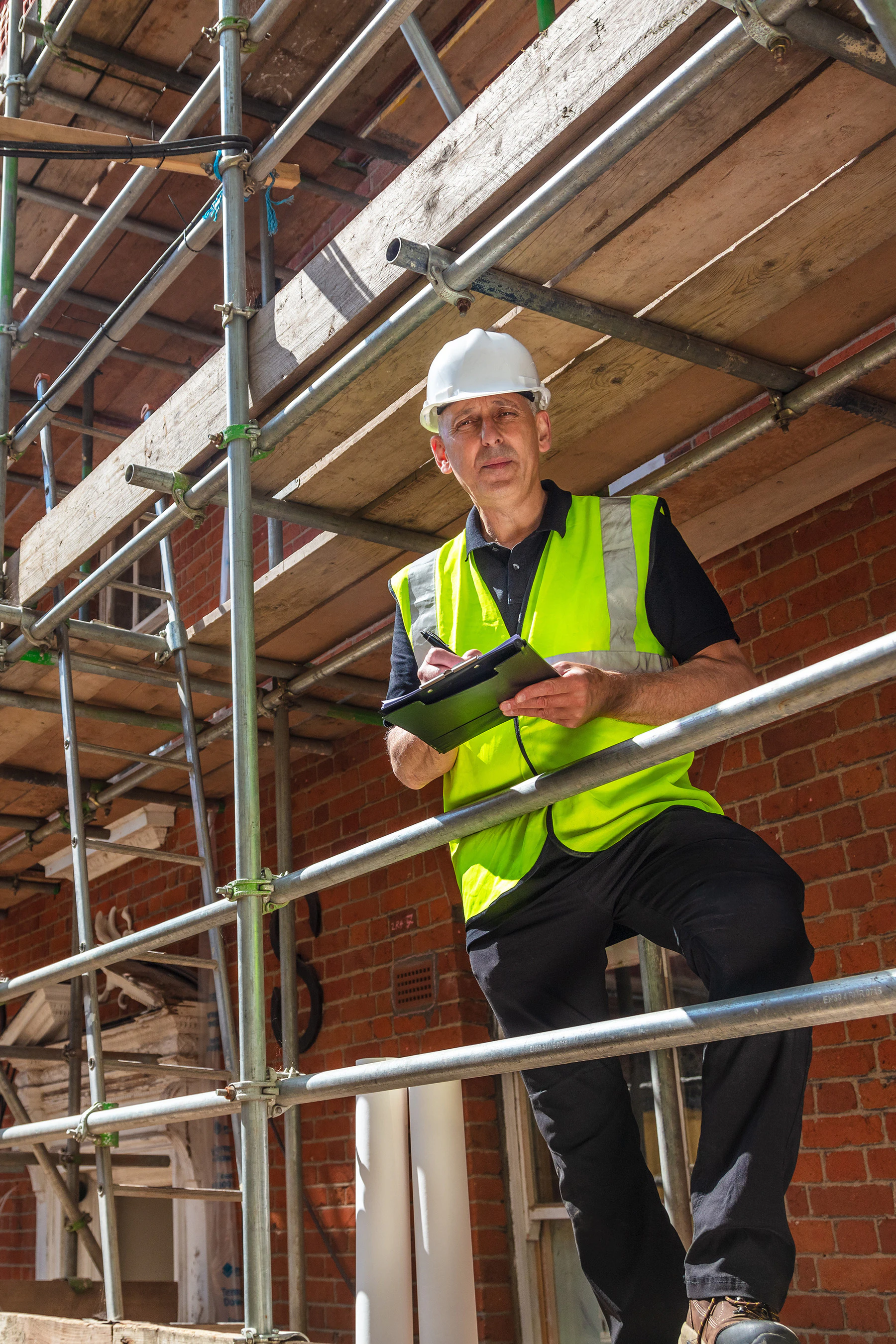 Construction worker assesses NYC scaffolding with a tablet, ensuring compliance with safety standards under Local Law 48 and Local Law 51 of 2025.